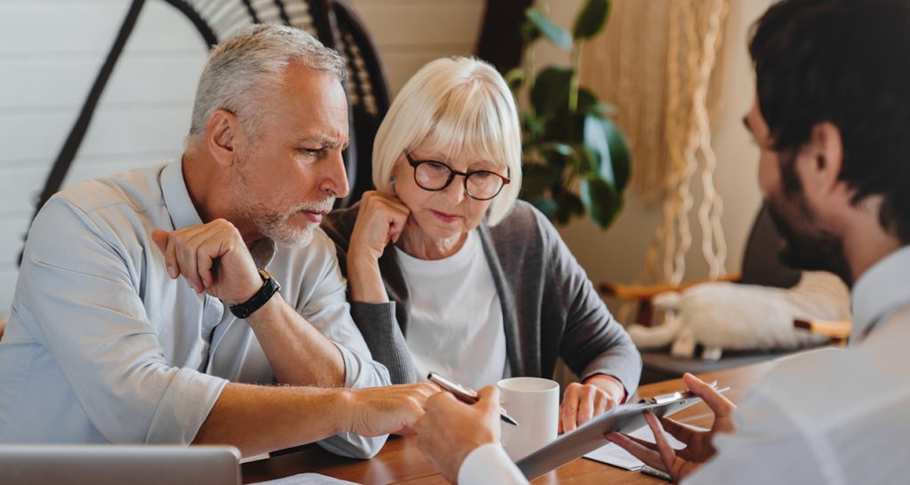 Certified financial planner explaining paperwork to elderly retired couple front of desk, 